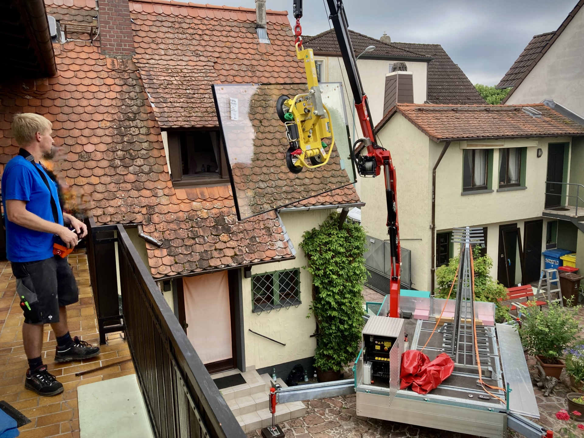 Ein Monteur steht auf einem Balkon und bedient mit einer Fernbedienung einen Kran, an dem eine große Glasfront hängt, die eingebaut wird