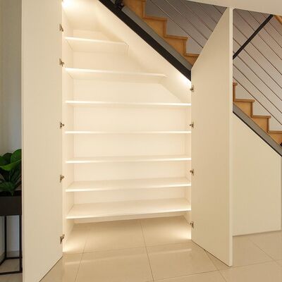 Begehbarer Schrank unter einer Treppe mit weißen Fronten und einem Regal, Türen offen